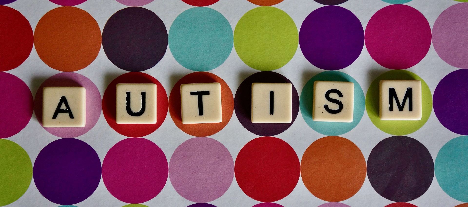the word "autism" is spelled out using scrabble square pieces on a coloured background of circles