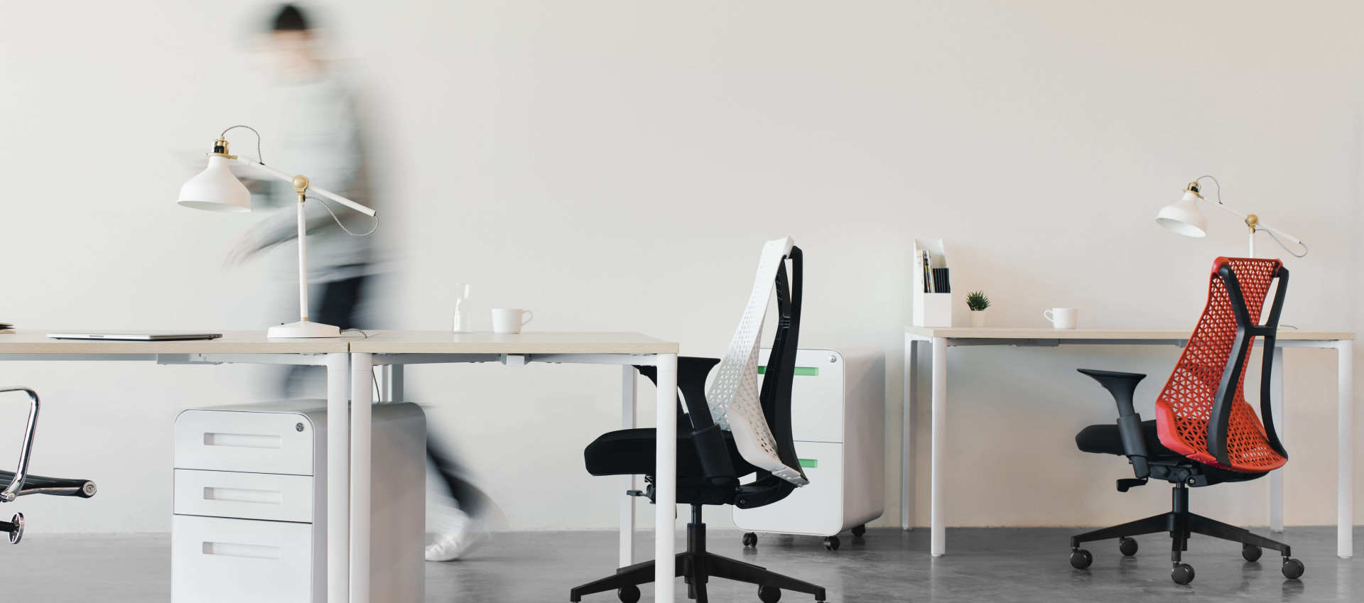 two office chairs and three desks with a blurred person in the background
