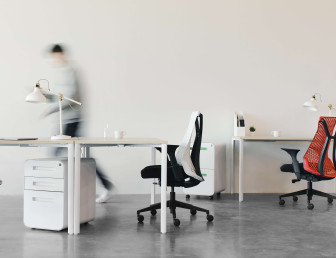 two office chairs and three desks with a blurred person in the background