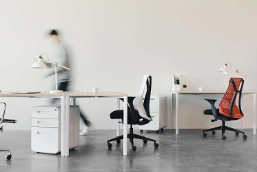 two office chairs and three desks with a blurred person in the background
