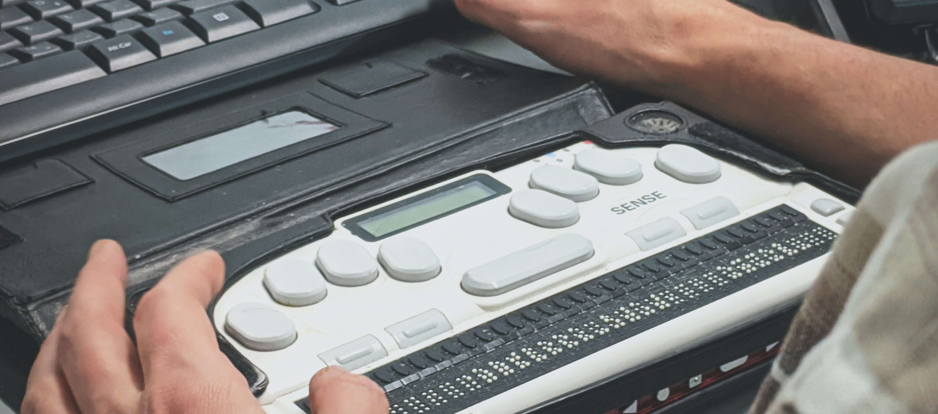 man's hands on a braille machine with a desktop keyword placed above