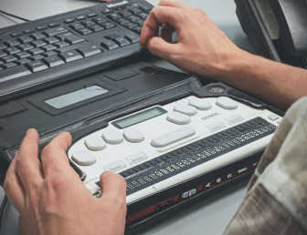 man's hands on a braille machine with a desktop keyword placed above