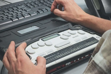 man's hands on a braille machine with a desktop keyword placed above