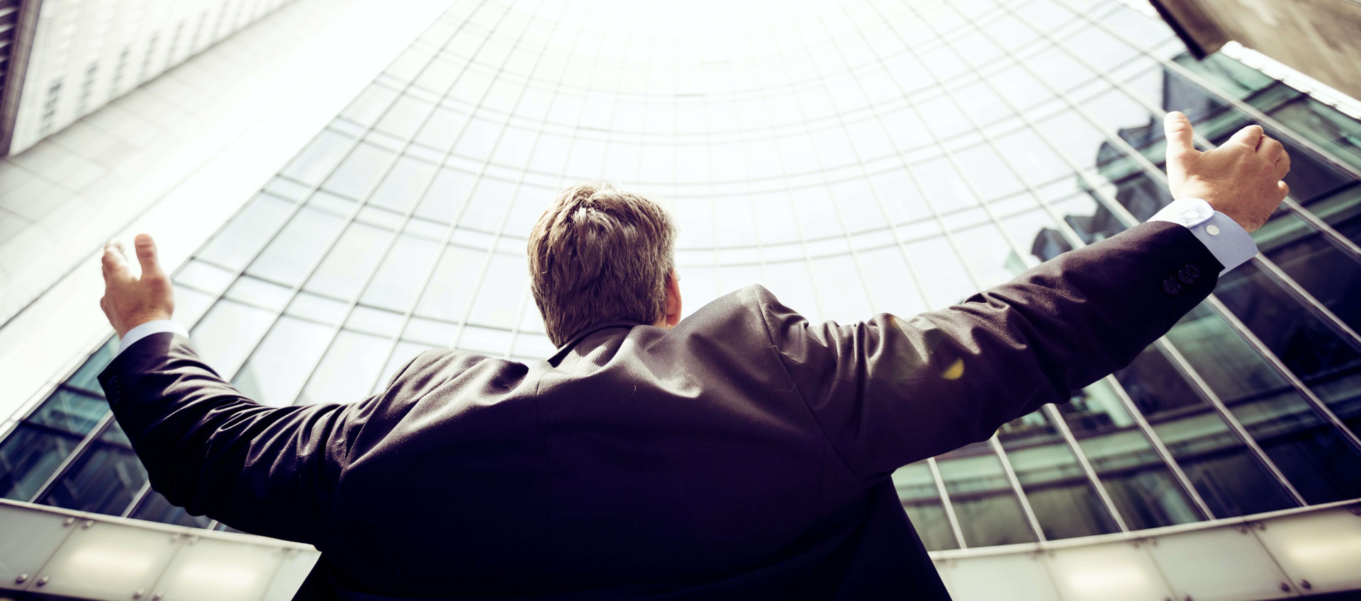 low angle view of man in suit with arms out wide towards the sky in front of high-rise buildings