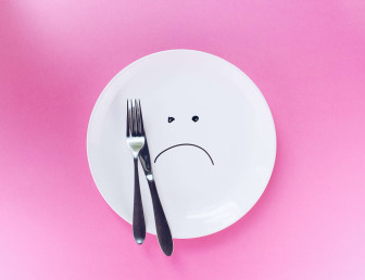 white plate with sad face with cutlery on pink background