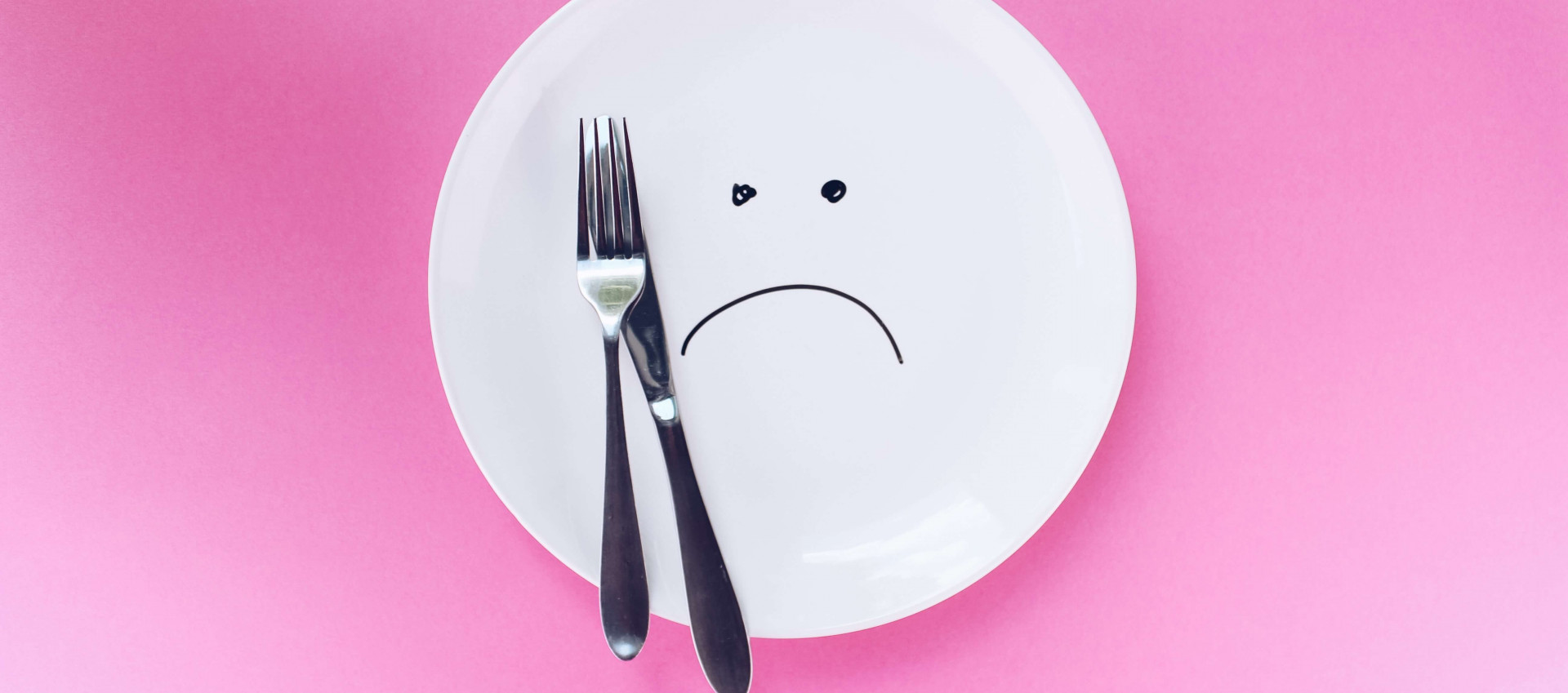 white plate with sad face with cutlery on pink background