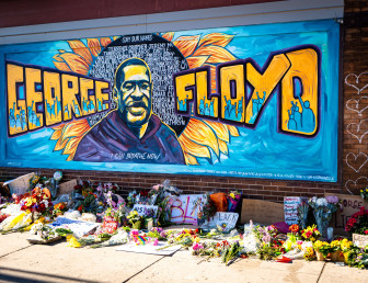 george floyd memorial on a brick wall with several flowers and messages on the sidewalk.