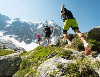 low angle view of three people running across rocks towards a snow-covered mountain