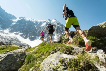 low angle view of three people running across rocks towards a snow-covered mountain