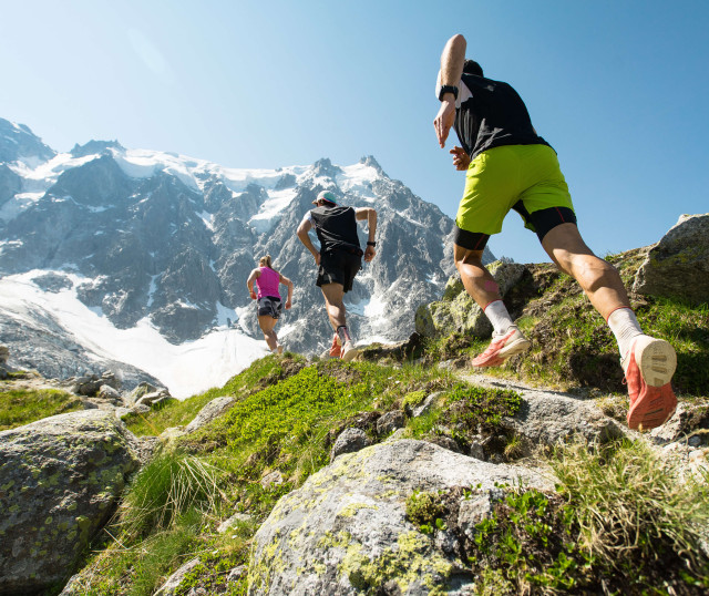 low angle view of three people running across rocks towards a snow-covered mountain