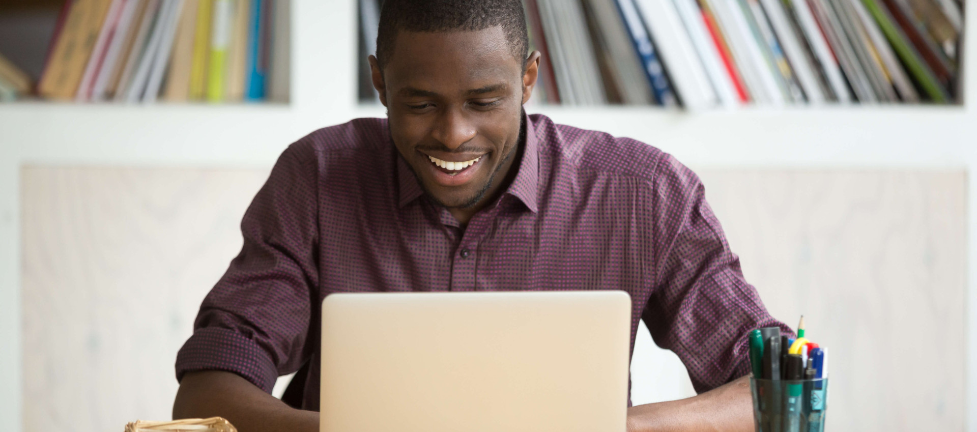 man smiling and sitting at a desk with laptop, pens and post-it notes on the table