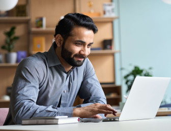 eye level view of bearded man in smart clothes smiling at laptop in an office