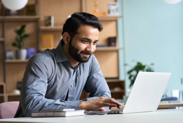 eye level view of bearded man in smart clothes smiling at laptop in an office