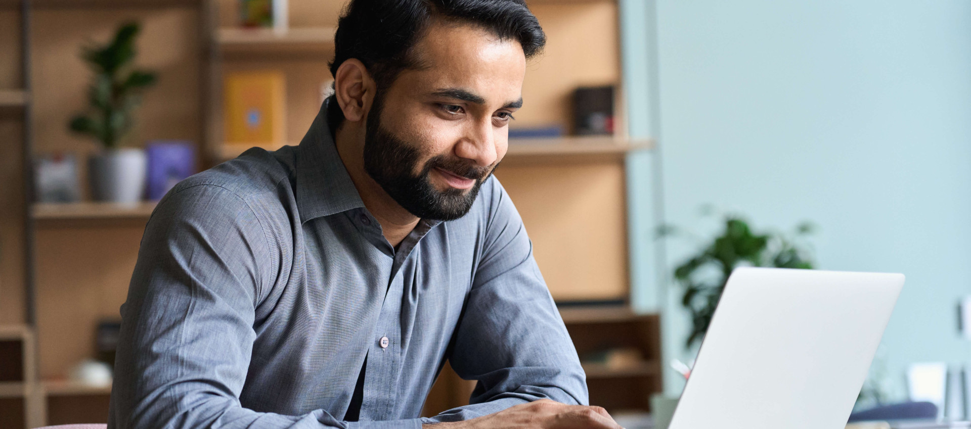 eye level view of bearded man in smart clothes smiling at laptop in an office