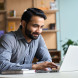 eye level view of bearded man in smart clothes smiling at laptop in an office