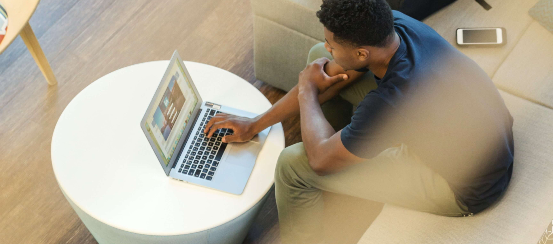 birds eye view of man wearing casual clothes sitting in lobby on a laptop with backpack on chair
