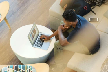 birds eye view of man wearing casual clothes sitting in lobby on a laptop with backpack on chair