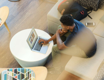 birds eye view of man wearing casual clothes sitting in lobby on a laptop with backpack on chair