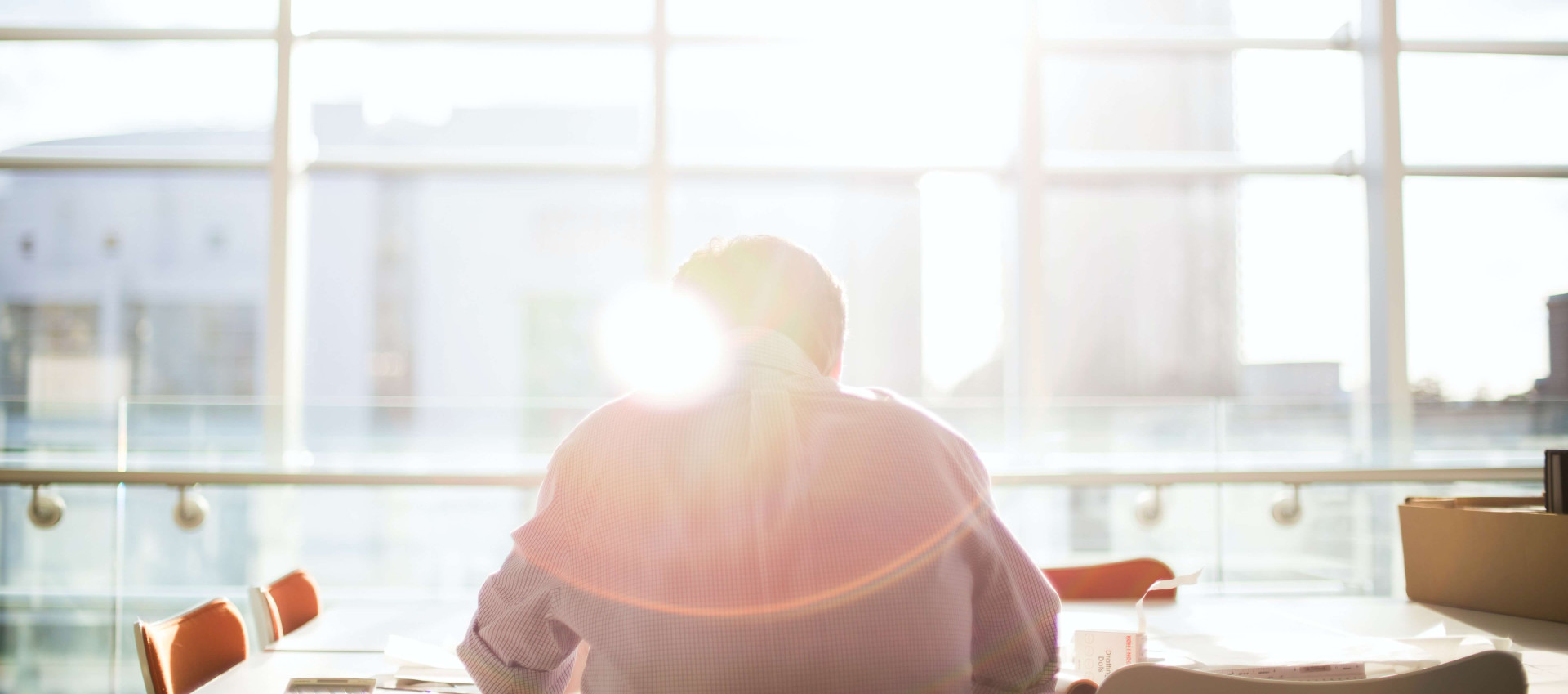 man sitting at an empty desk in front of large window with a slight glare from the sun