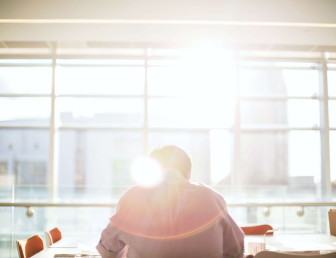 man sitting at an empty desk in front of large window with a slight glare from the sun