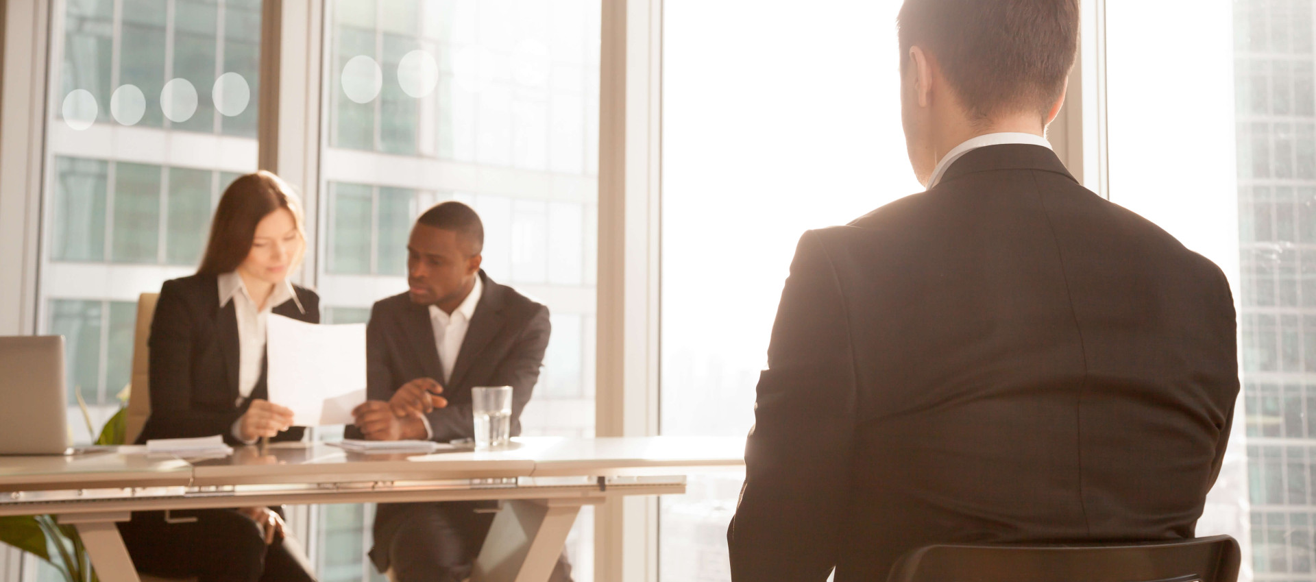 man in an interview in front of two business people looking at a document in a corporate setting