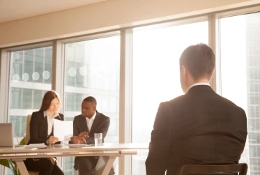 man in an interview in front of two business people looking at a document in a corporate setting