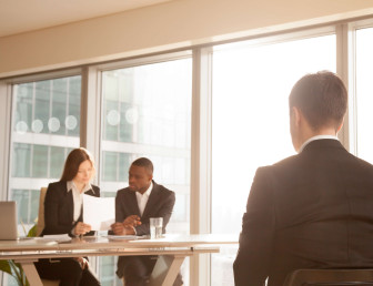 man in an interview in front of two business people looking at a document in a corporate setting