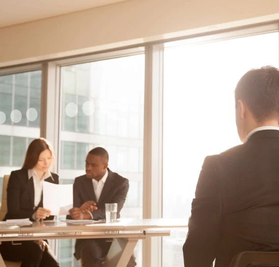 man in an interview in front of two business people looking at a document in a corporate setting