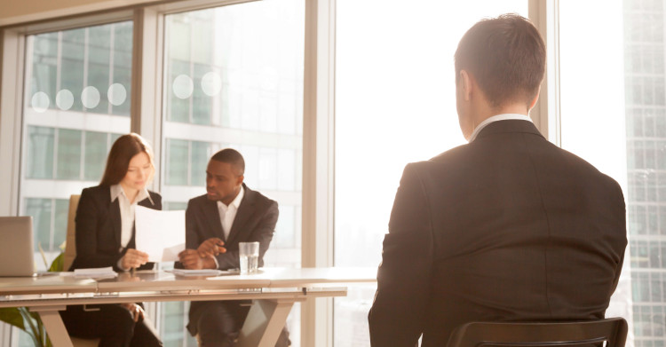 man in an interview in front of two business people looking at a document in a corporate setting