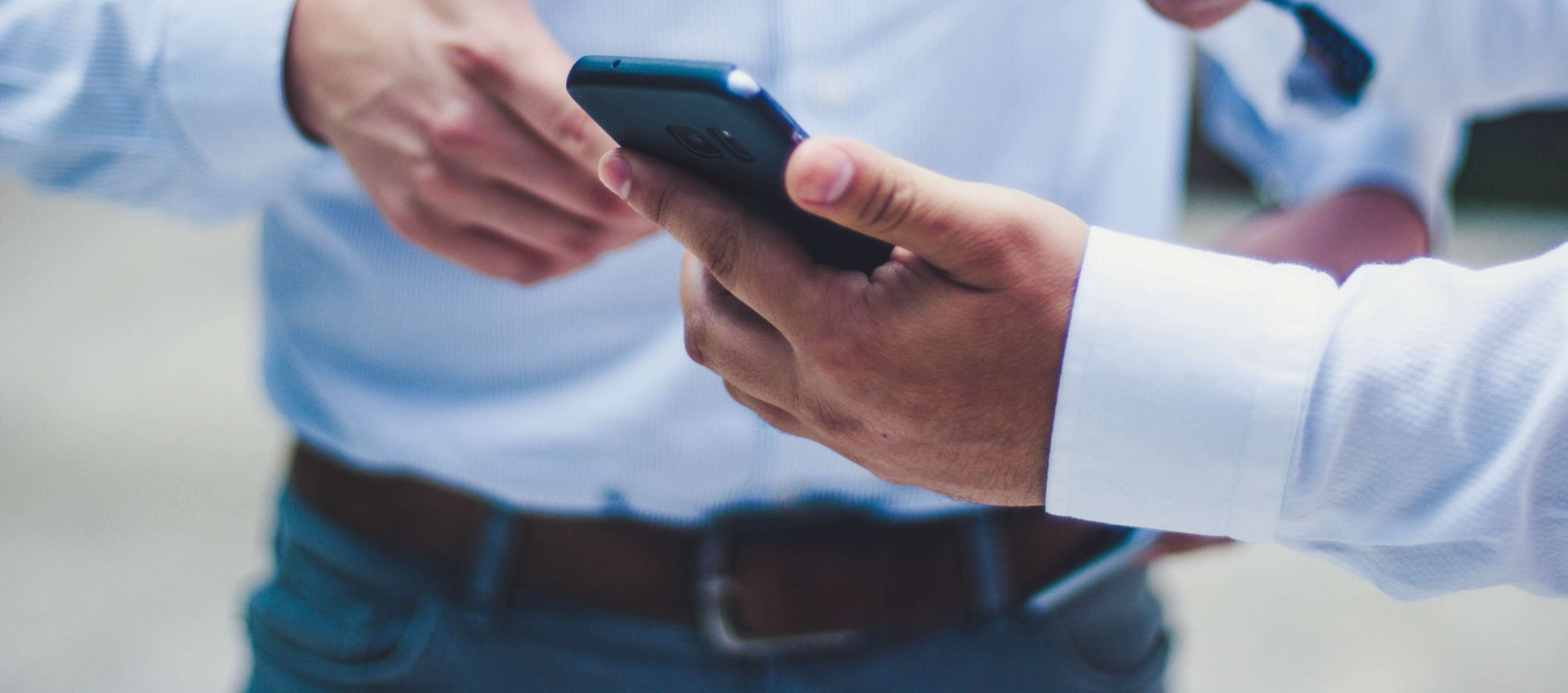 two men wearing smart clothing with one man holding and pointing at mobile phone