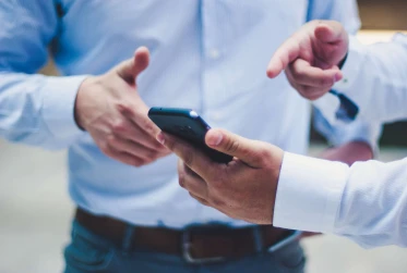 two men wearing smart clothing with one man holding and pointing at mobile phone