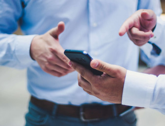two men wearing smart clothing with one man holding and pointing at mobile phone