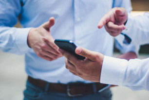 two men wearing smart clothing with one man holding and pointing at mobile phone