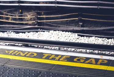 the word "mind the gap" in yellow writing on the floor with electric train wiring in the background