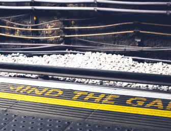 the word "mind the gap" in yellow writing on the floor with electric train wiring in the background