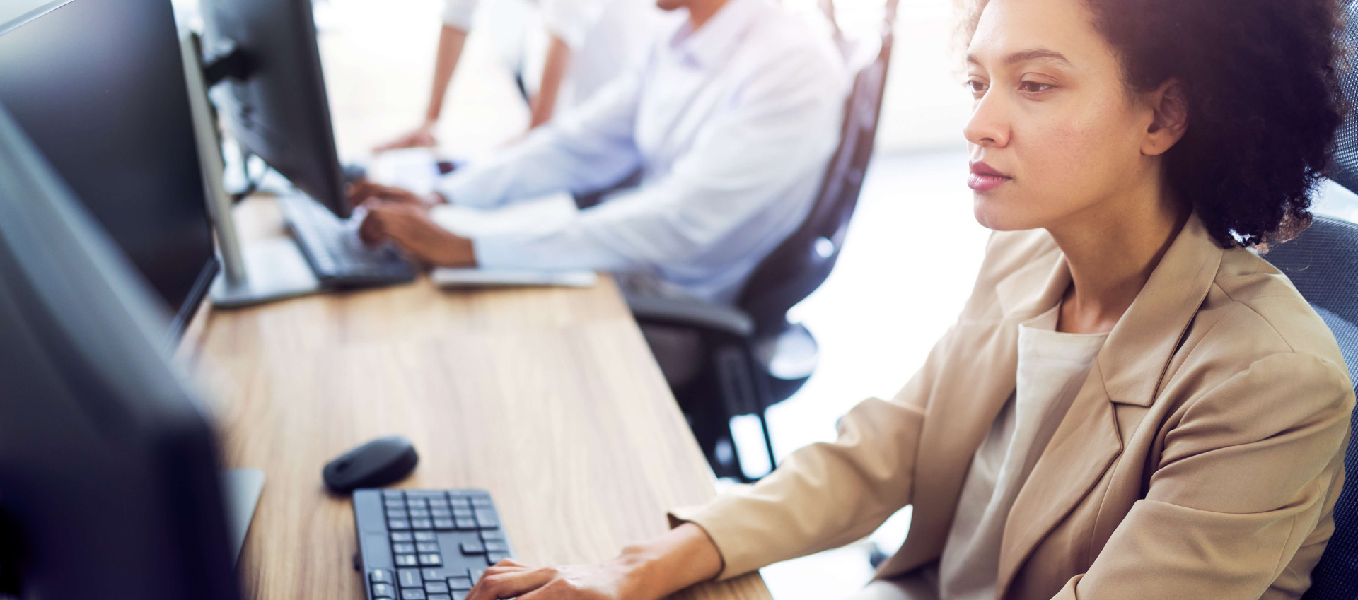 side view of woman in smart clothing working at a desk with two people blurred in the background