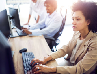 side view of woman in smart clothing working at a desk with two people blurred in the background