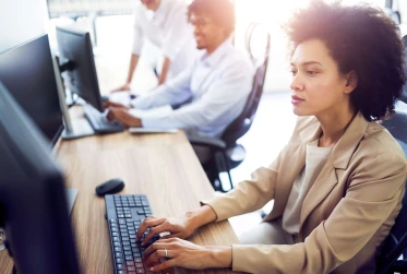 side view of woman in smart clothing working at a desk with two people blurred in the background