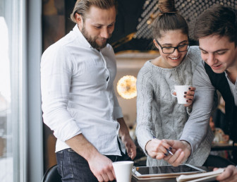 A group of four colleague in an office setting. They are gather around a table covered with work-related documents. 