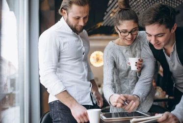 A group of four colleague in an office setting. They are gather around a table covered with work-related documents. 