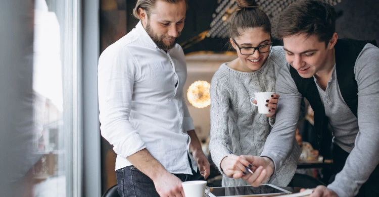A group of four colleague in an office setting. They are gather around a table covered with work-related documents. 