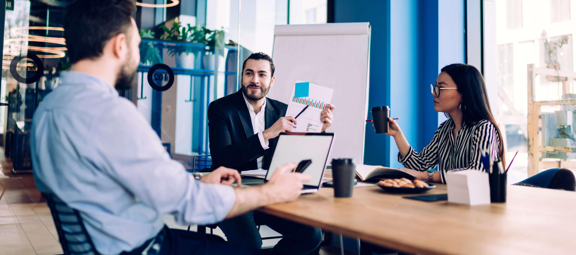 three people in a meeting wearing smart clothing with a man pointing to a document