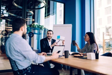 three people in a meeting wearing smart clothing with a man pointing to a document