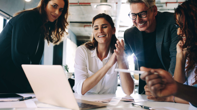 eye level view of four people smiling and wearing smart clothing surrounding laptop