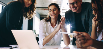 eye level view of four people smiling and wearing smart clothing surrounding laptop