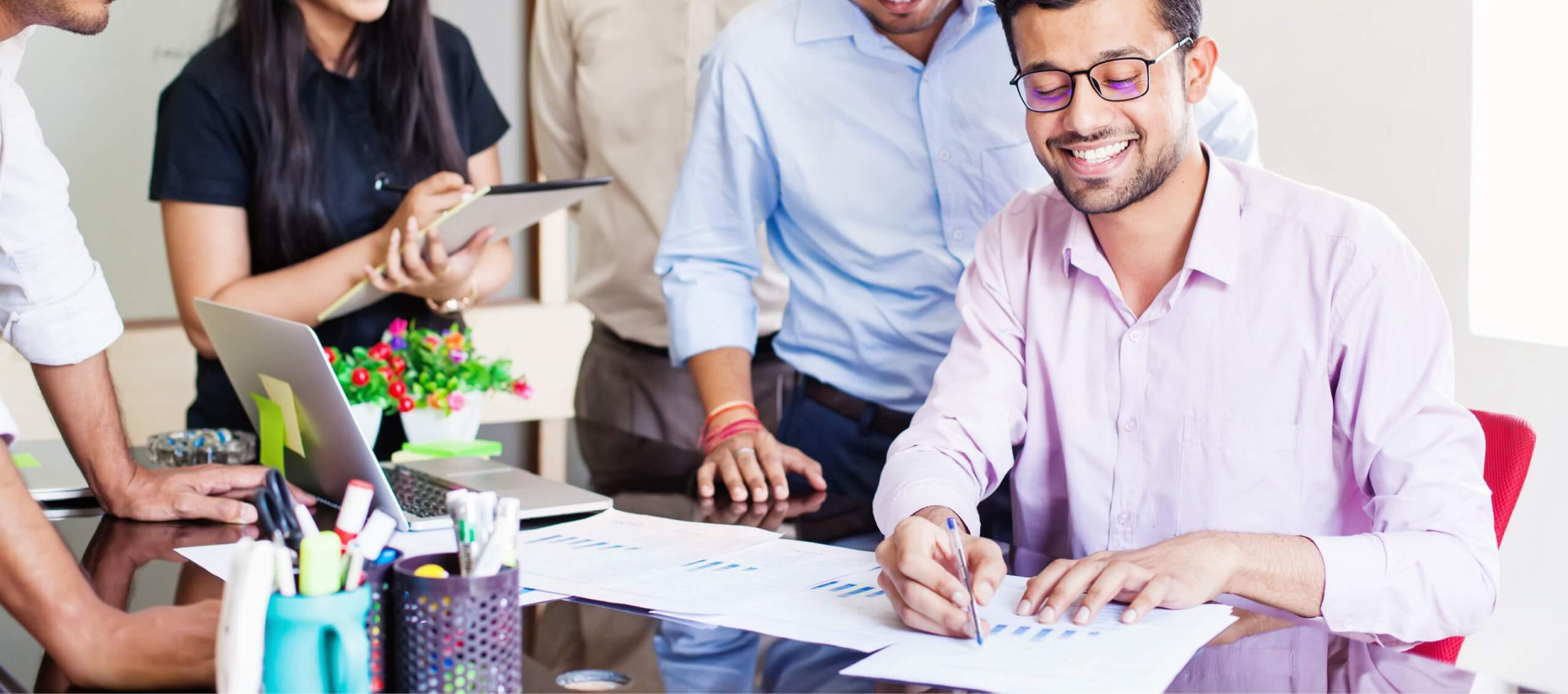 one person smiling and writing on paper with onlookers smiling