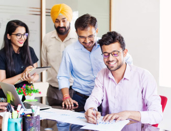 one person smiling and writing on paper with onlookers smiling