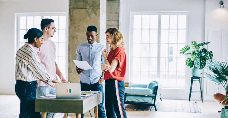four people in gathered round a small table with a laptop in a casual office setting