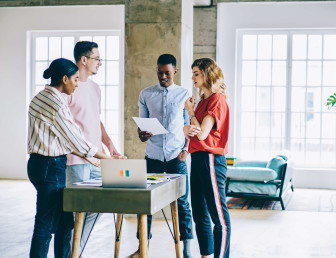 four people in gathered round a small table with a laptop in a casual office setting