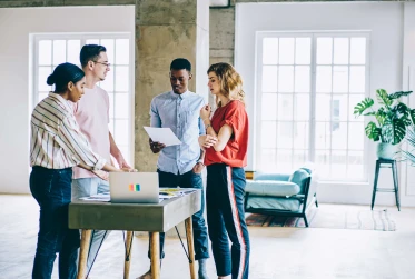 four people in gathered round a small table with a laptop in a casual office setting